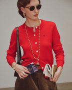 Woman wearing a red cardigan holding books and a passport against a plain background