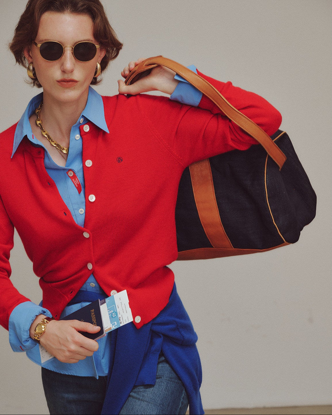 Woman wearing a red sweater over a blue shirt, holding a black and brown bag.