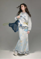 Woman wearing a floral outfit with a blue bag against a gray background