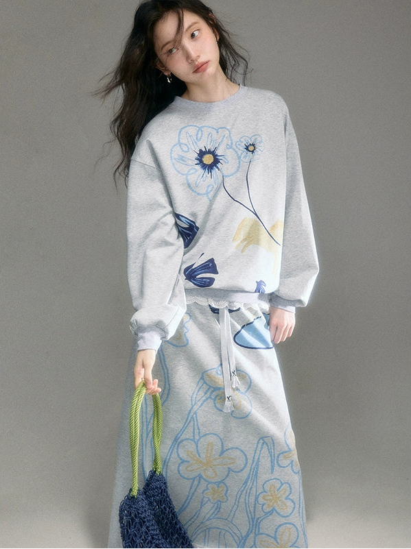 Woman wearing a gray sweatshirt and skirt with floral patterns on a gray background