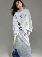 Woman wearing a gray sweatshirt and skirt with floral patterns on a gray background