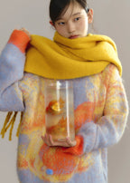 Person wearing a colorful sweater and yellow scarf holding a glass container with a goldfish.