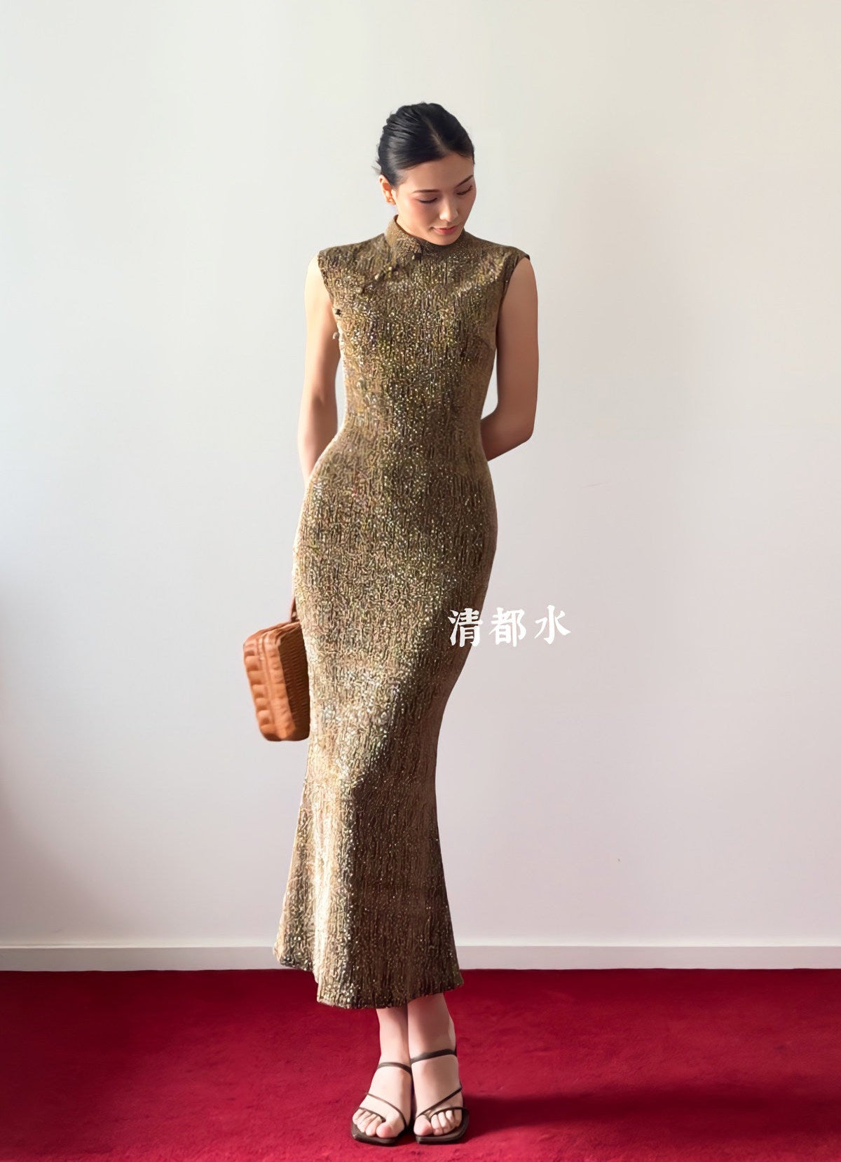 Woman in a gold dress standing on a red carpet with a white wall background