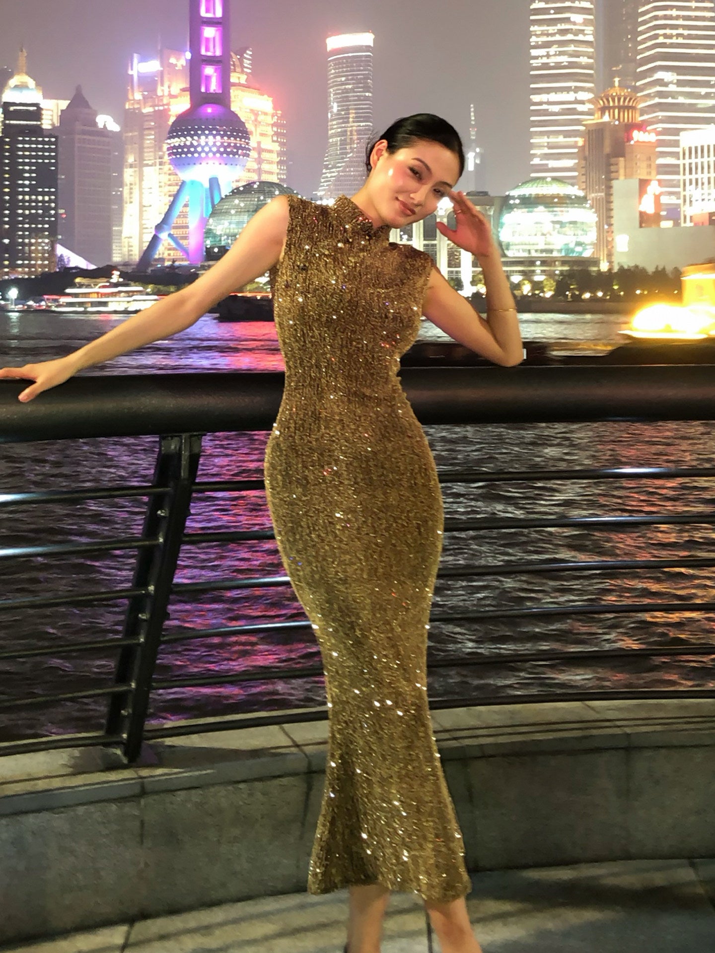 Woman in a gold sequin dress against a city skyline at night.