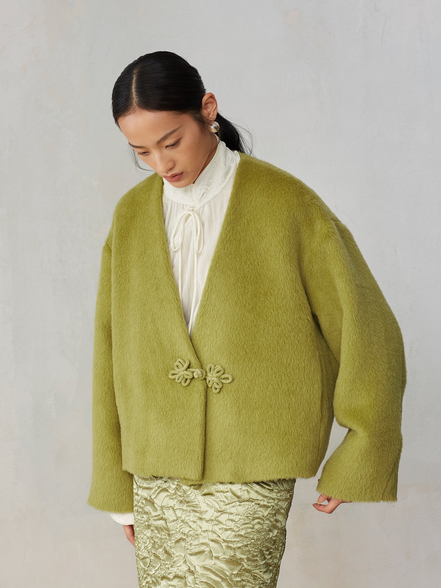 Person wearing a green cardigan with floral details on a plain background