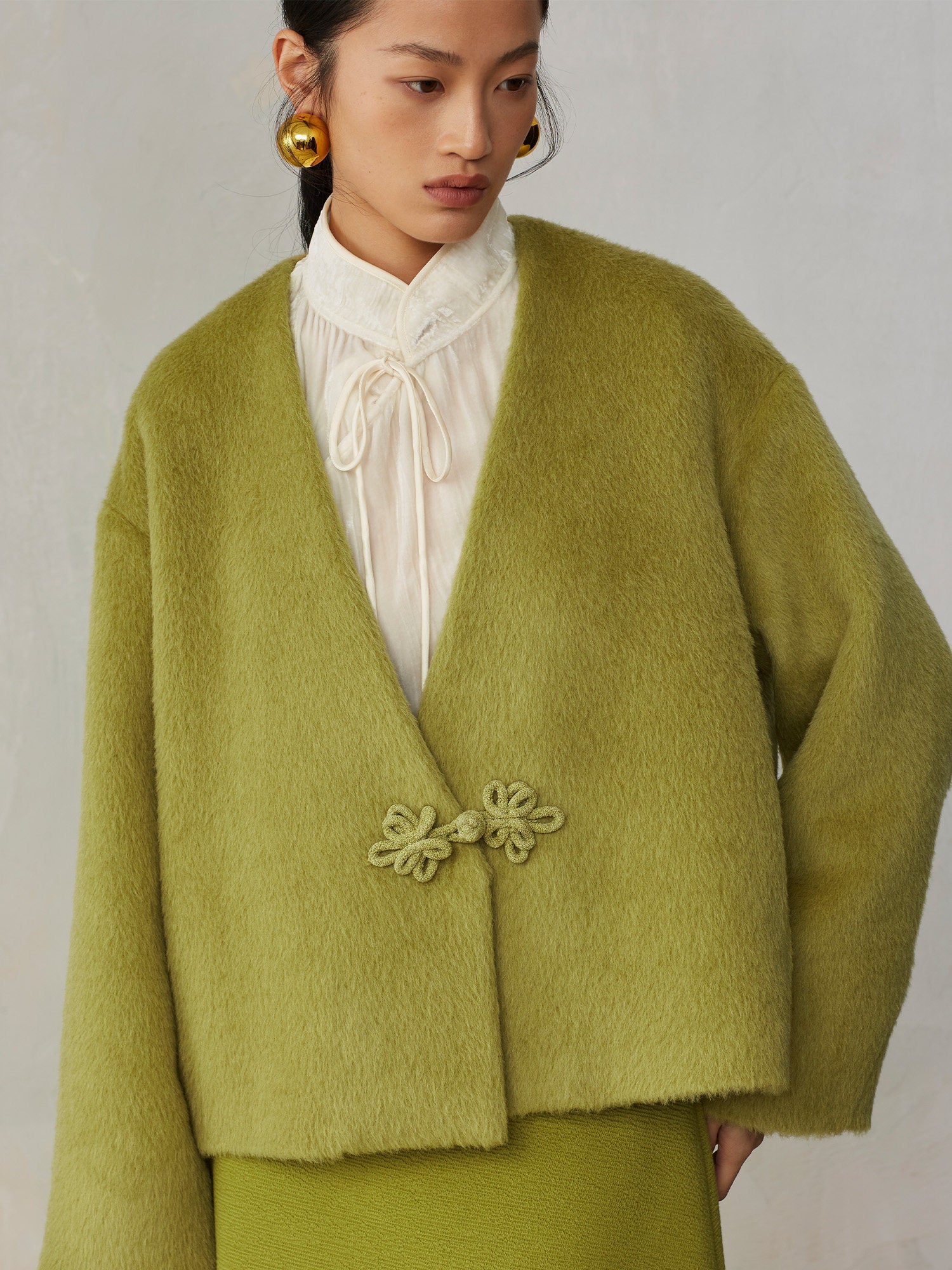 Woman wearing a green cardigan with floral details on a plain background