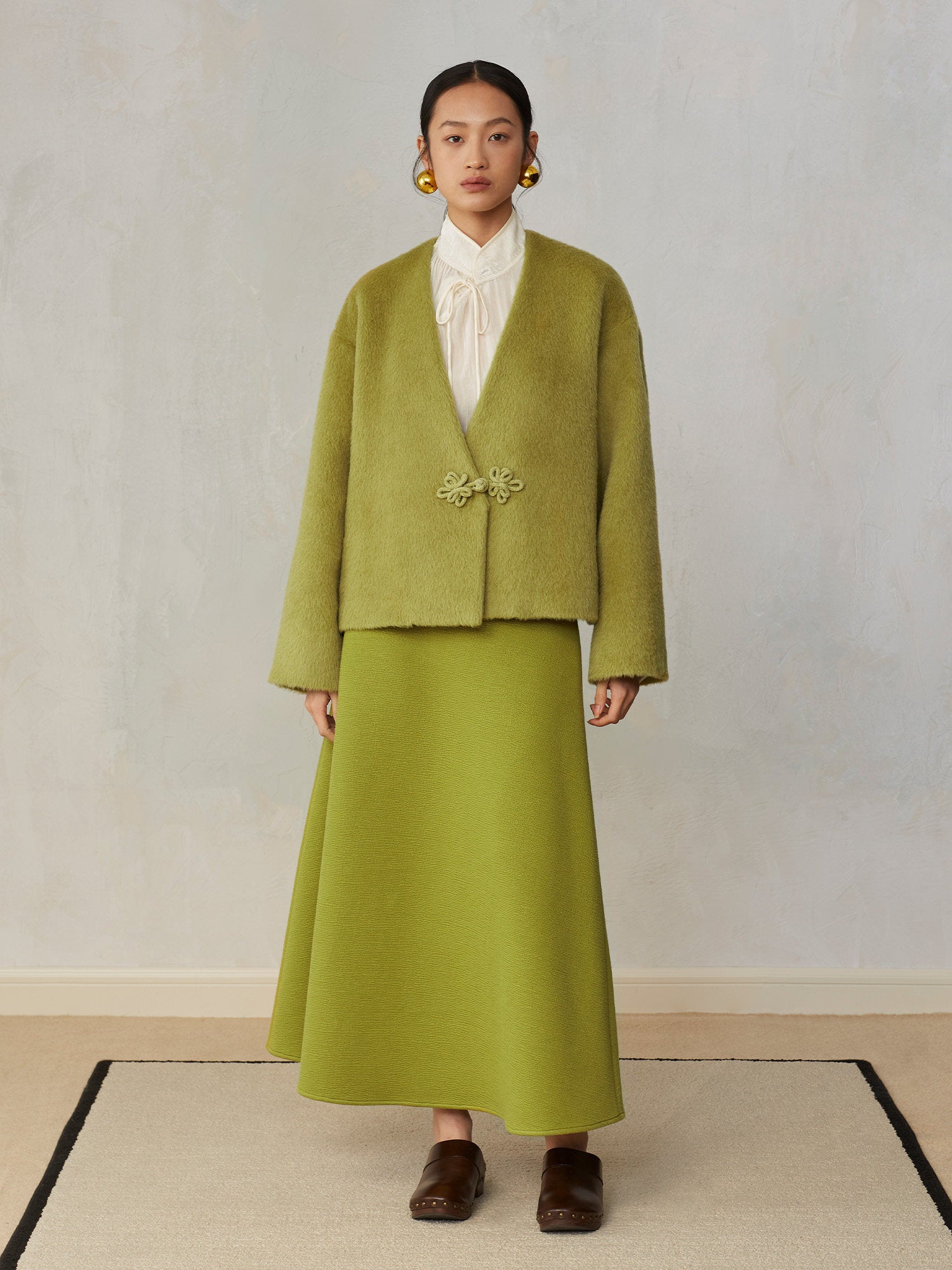 Woman wearing a green outfit with a white blouse against a plain background