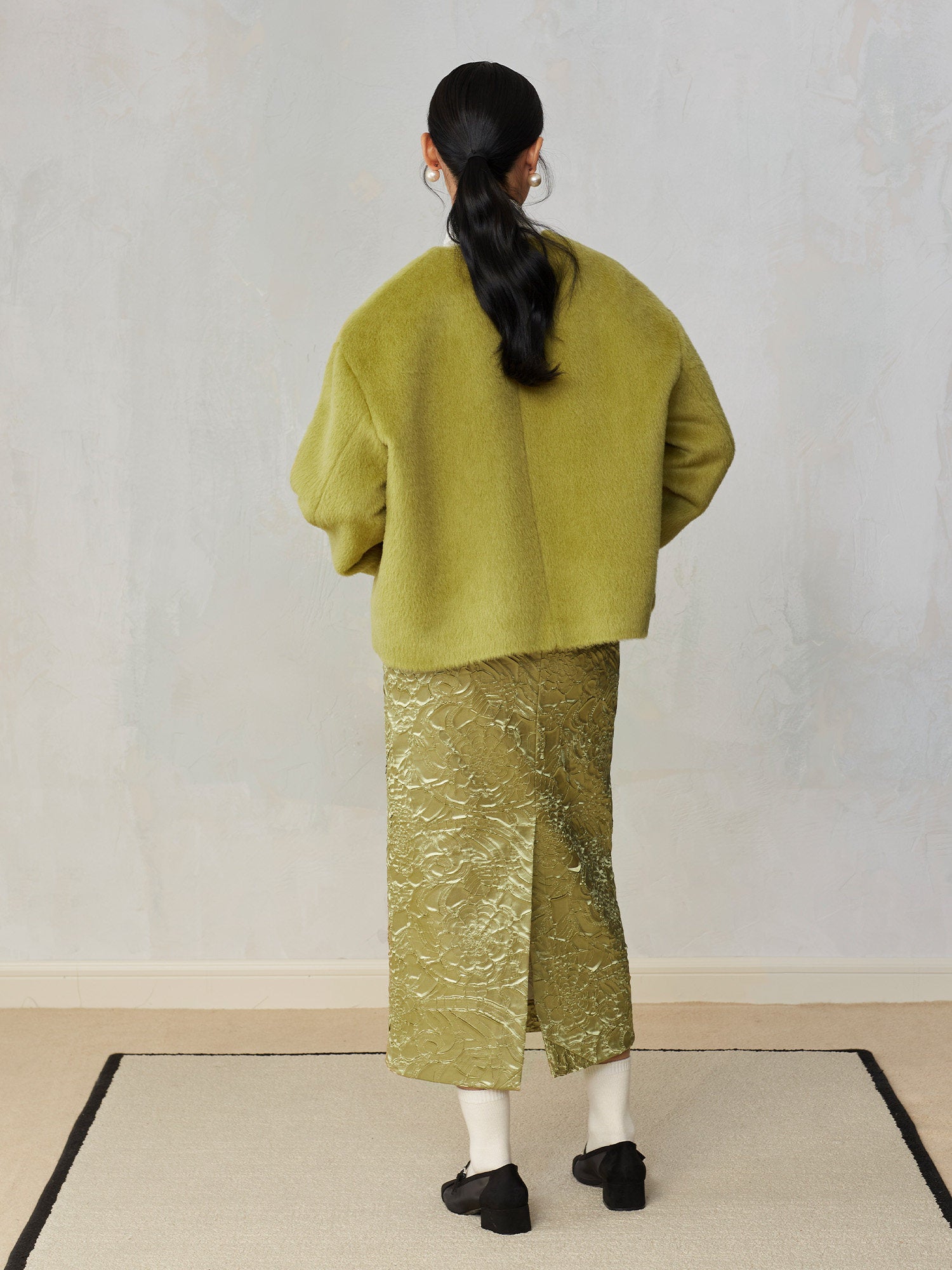 Person wearing a green outfit with a textured skirt against a plain background