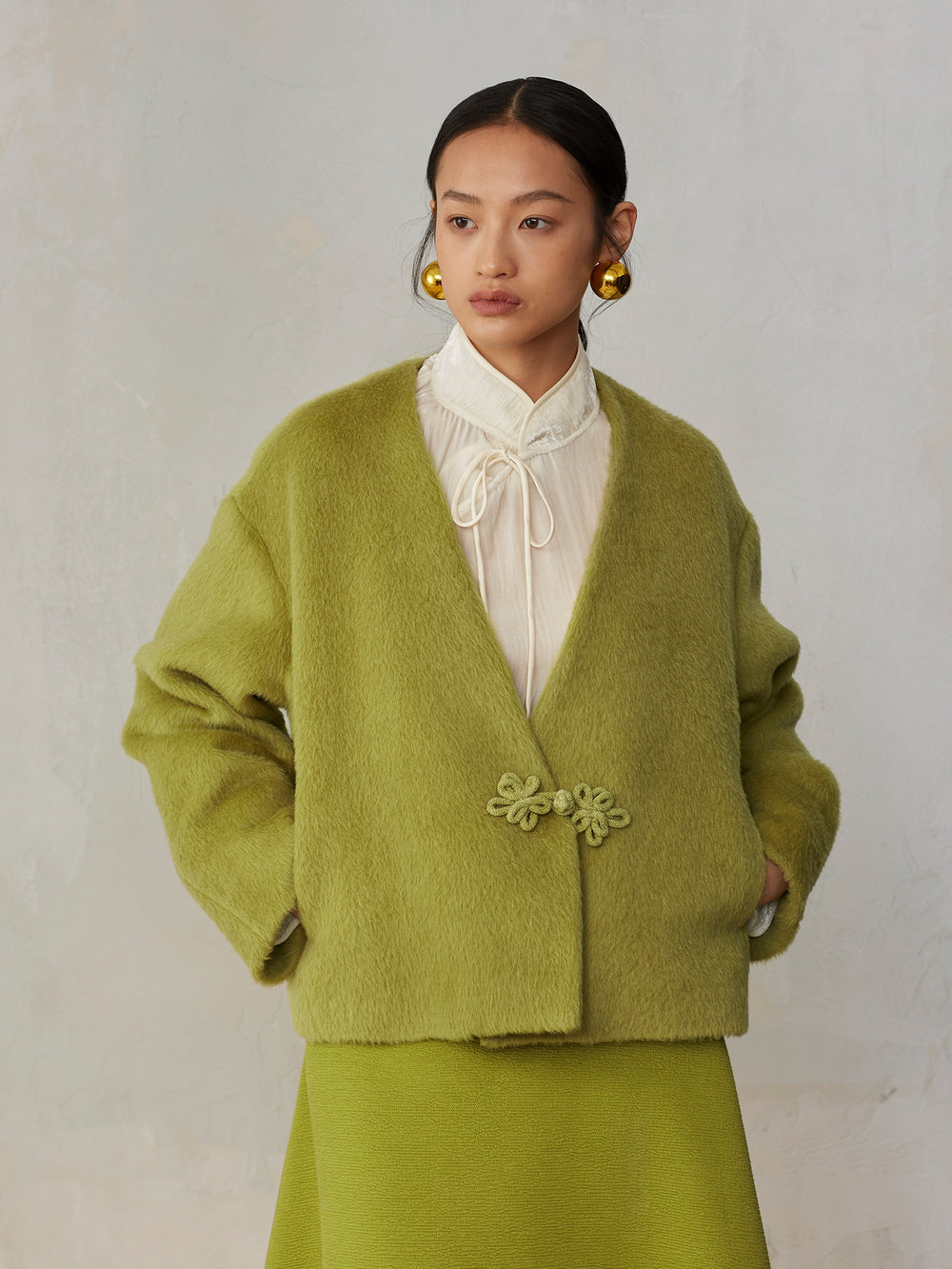 Woman wearing a green cardigan with floral details on a plain background