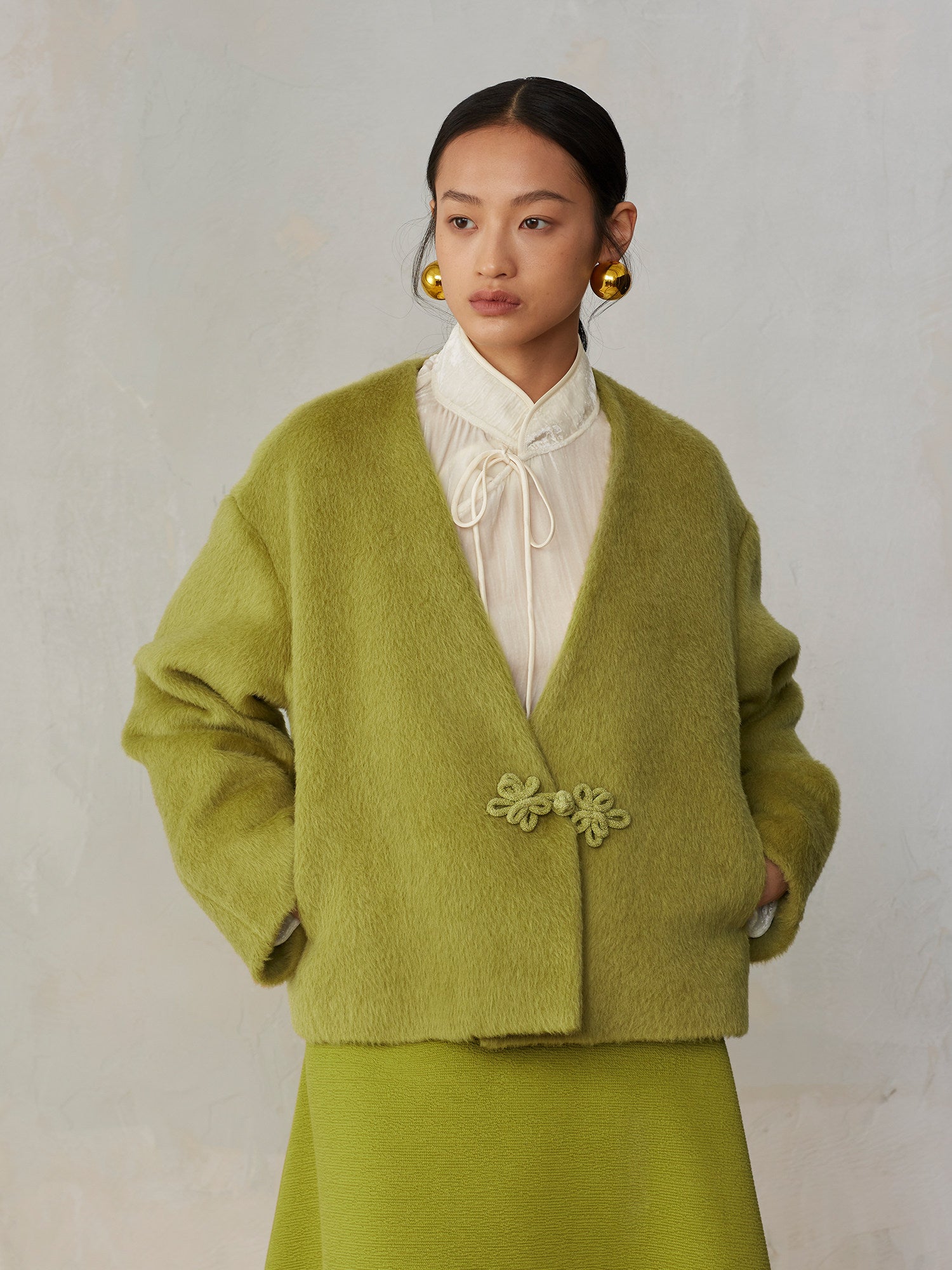 Woman wearing a green cardigan with floral details on a plain background