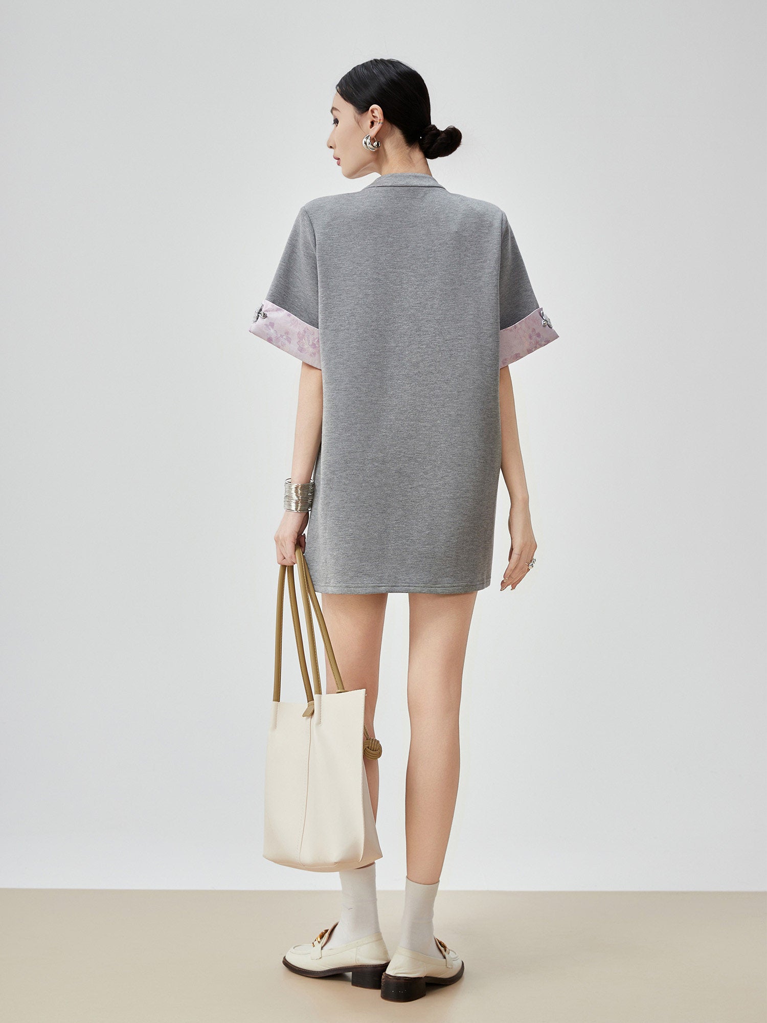 Person wearing a gray dress with pink accents, holding a white bag on a plain background