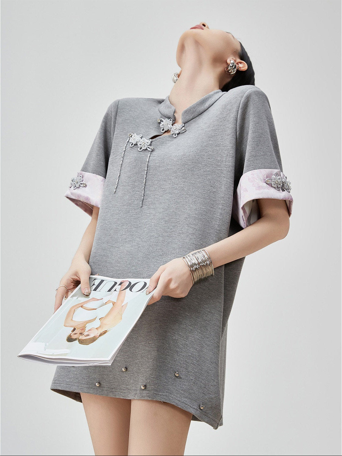 Woman wearing a gray dress with decorative elements, holding a magazine.