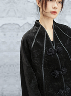 Person wearing a black velvet coat with floral buttons against a textured gray background