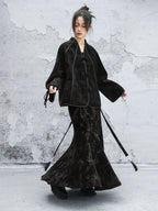 Person wearing a black outfit with long sleeves and a skirt against a textured gray wall.