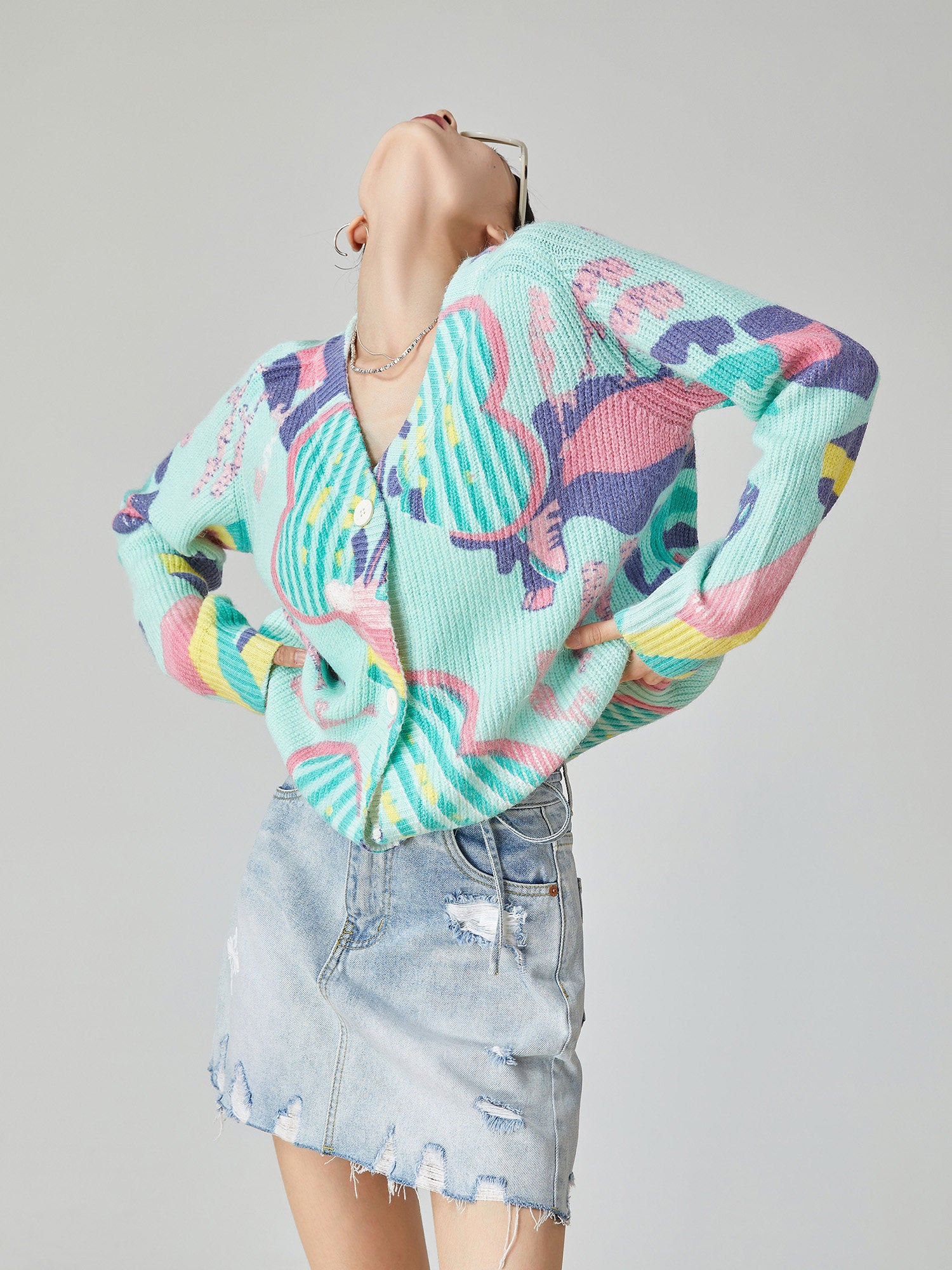 Person wearing a colorful patterned sweater and denim skirt on a plain background