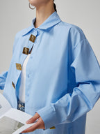 Light blue shirt with gold buttons worn by a person on a gray background