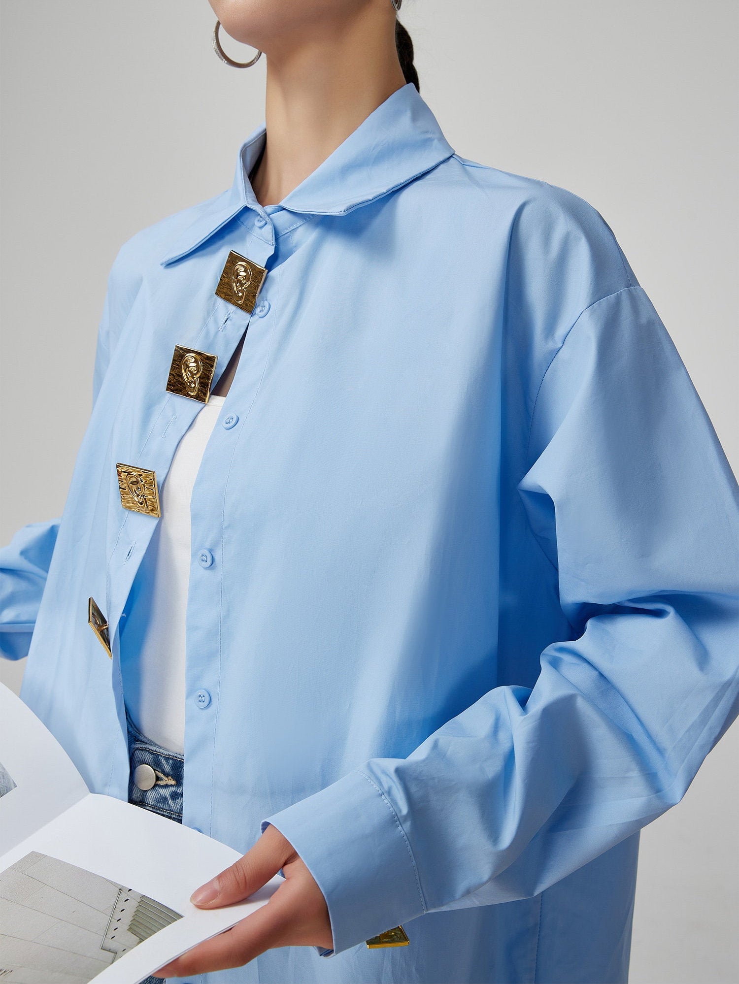 Light blue shirt with gold buttons worn by a person on a gray background