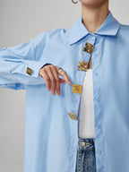 Light blue shirt with gold buttons worn by a person on a gray background