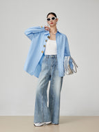 woman wearing a light blue denim jacket, white top, and jeans with a neutral background