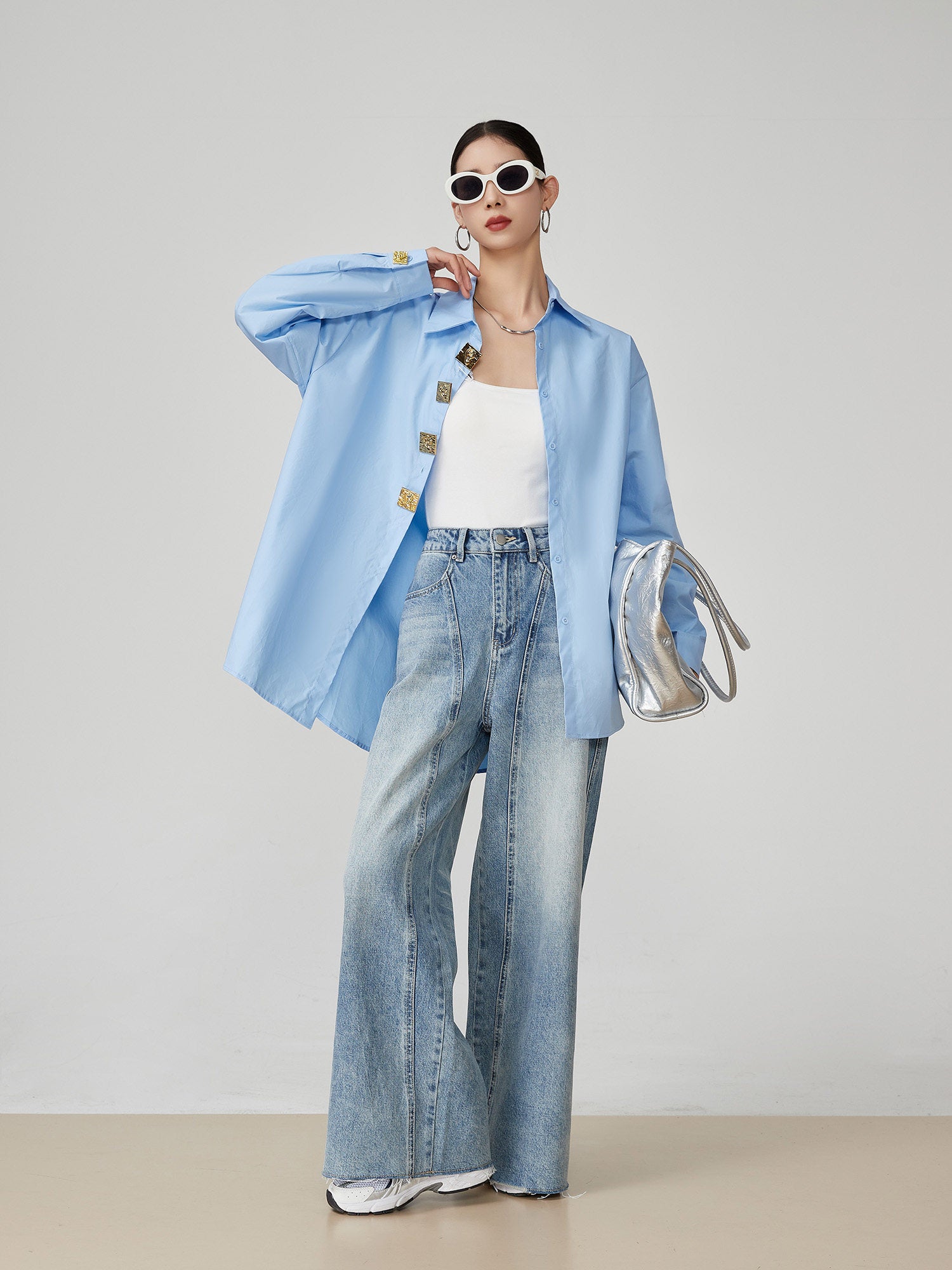 woman wearing a light blue denim jacket, white top, and jeans with a neutral background