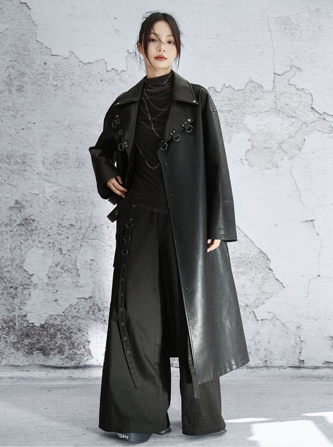 Person wearing a long black coat against a textured gray wall.