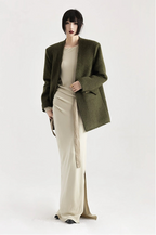 Person wearing a green coat over a beige outfit on a white background