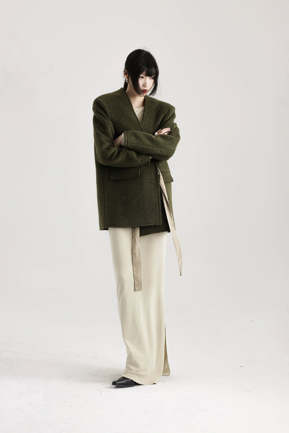 Person wearing a green coat and beige pants on a white background