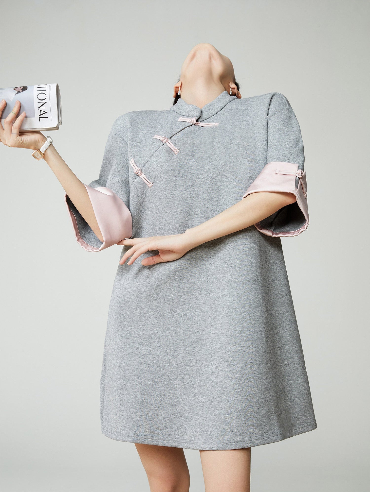 Woman wearing a grey dress with pink accents, holding a magazine.