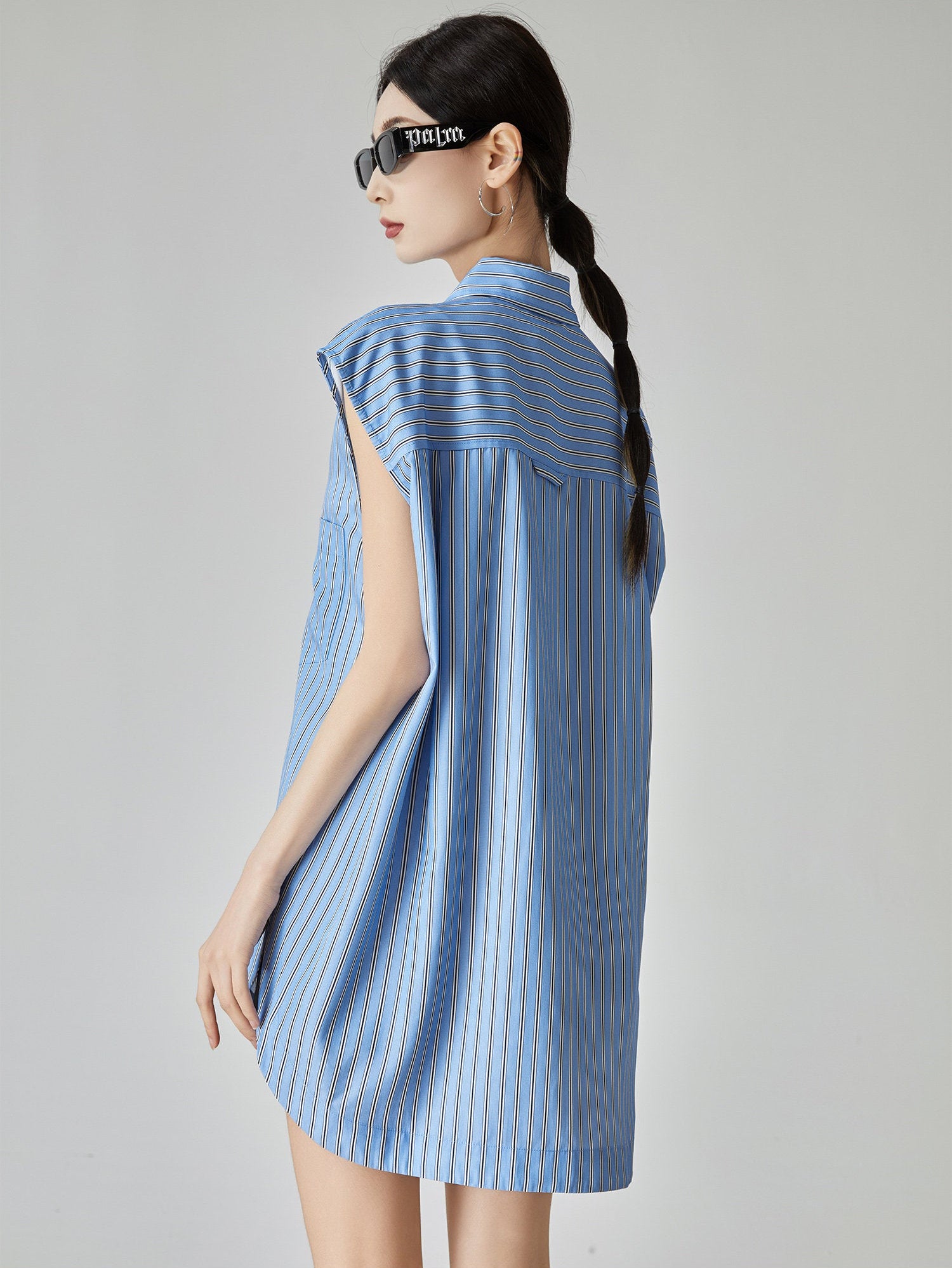 Woman wearing a blue striped dress with sunglasses on a gray background