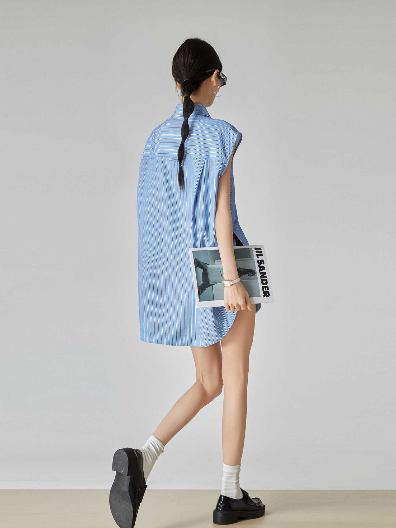 Woman wearing a light blue sleeveless shirt holding a magazine against a plain background