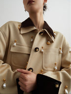 Close-up of a person wearing a beige coat with decorative buttons on a plain background