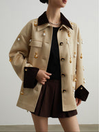 Person wearing a beige trench coat with gold buttons on a plain background