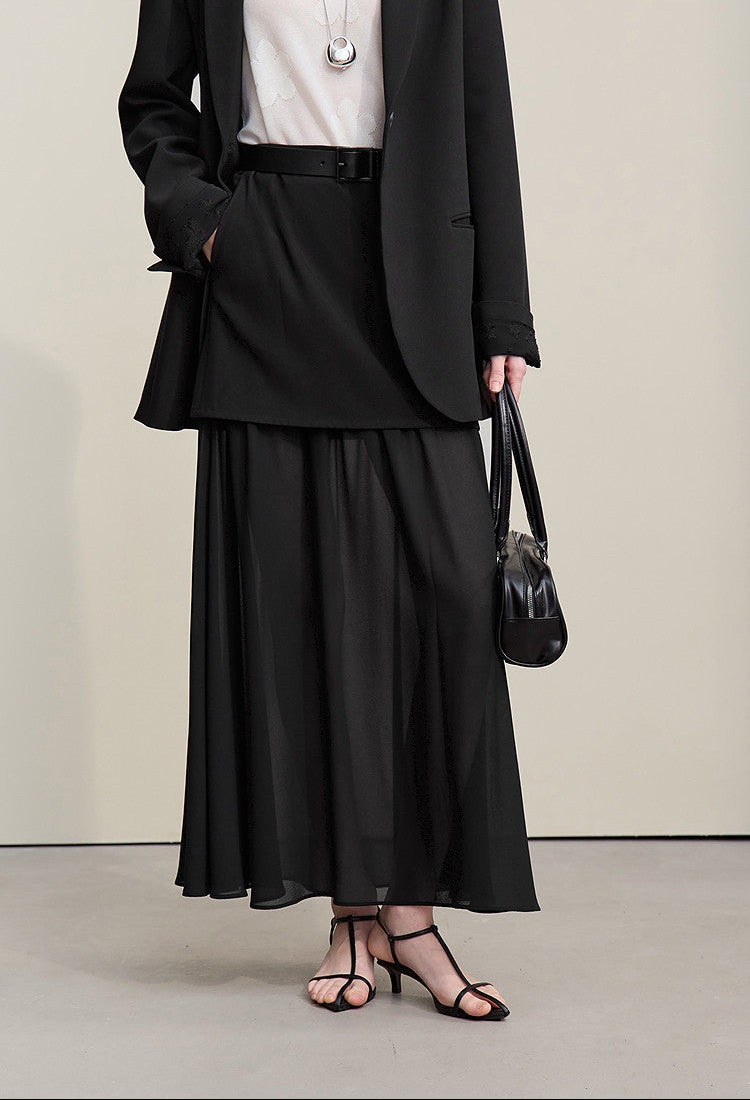 Person wearing a black suit with a white shirt and holding a black handbag on a plain background