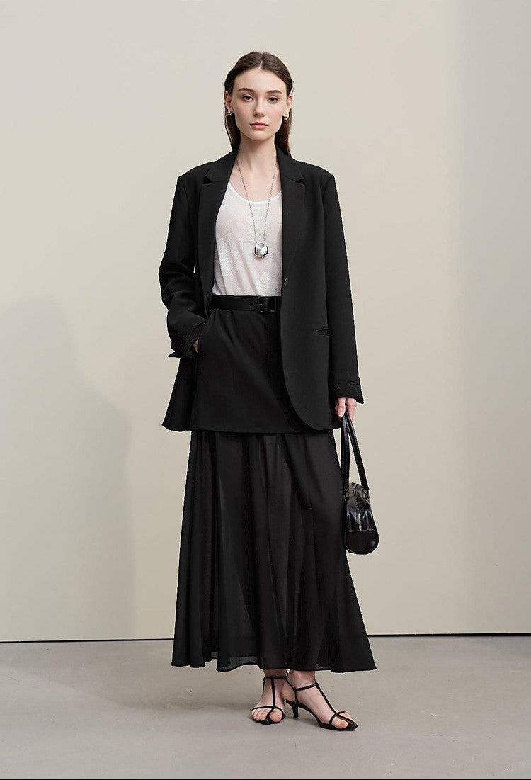 Woman wearing a black blazer and skirt with a white top, standing against a plain background.