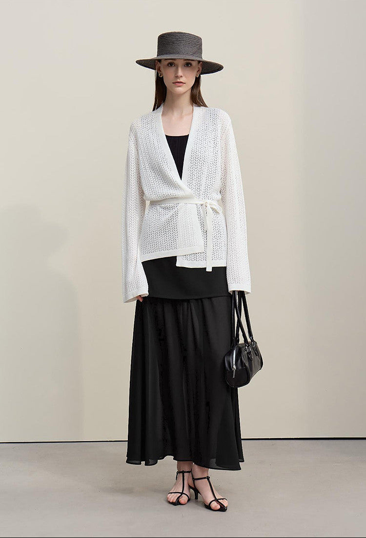 Woman wearing a white top, black skirt, and hat with a handbag on a plain background