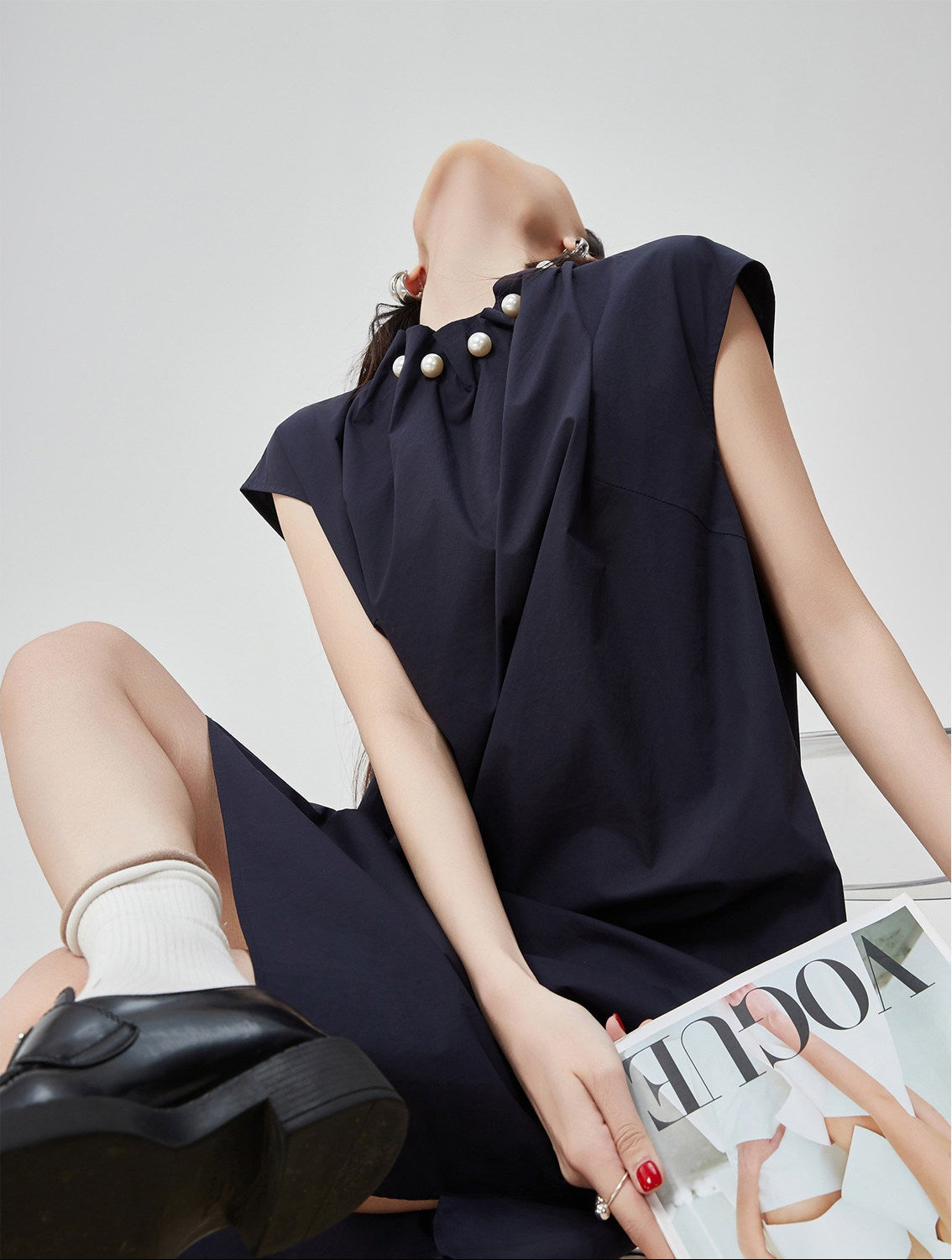 Woman wearing a dark blue dress with pearl embellishments, sitting on a white surface.