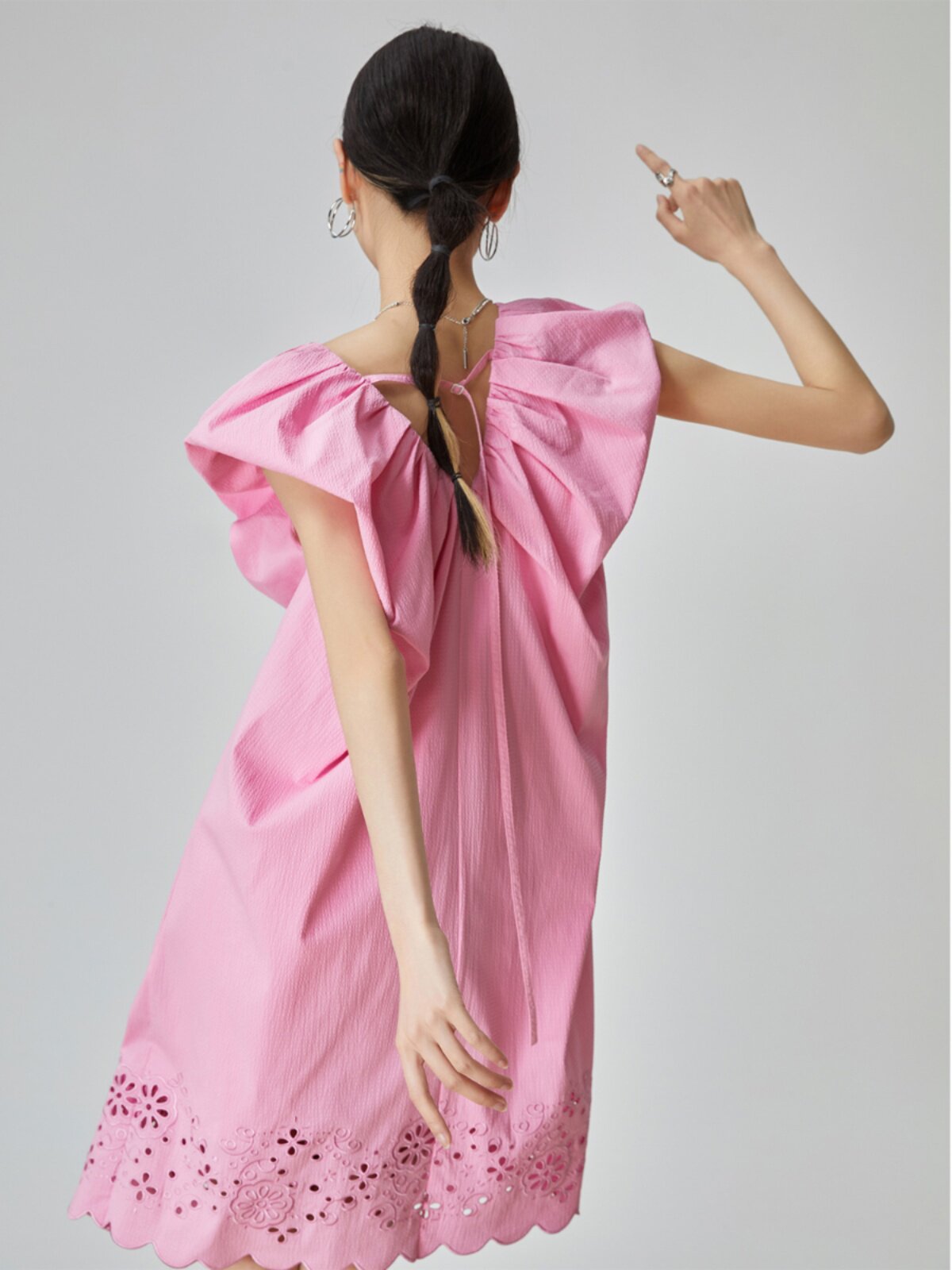 Woman wearing a pink dress with ruffled sleeves and lace details on a gray background