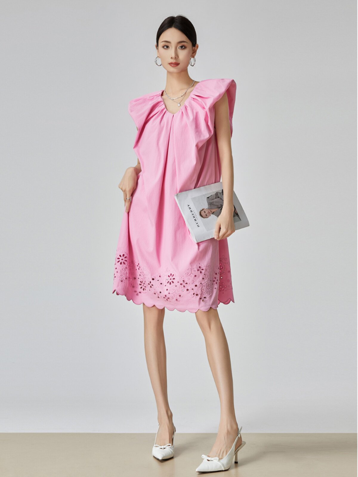 Woman wearing a pink dress with ruffled shoulders against a plain background