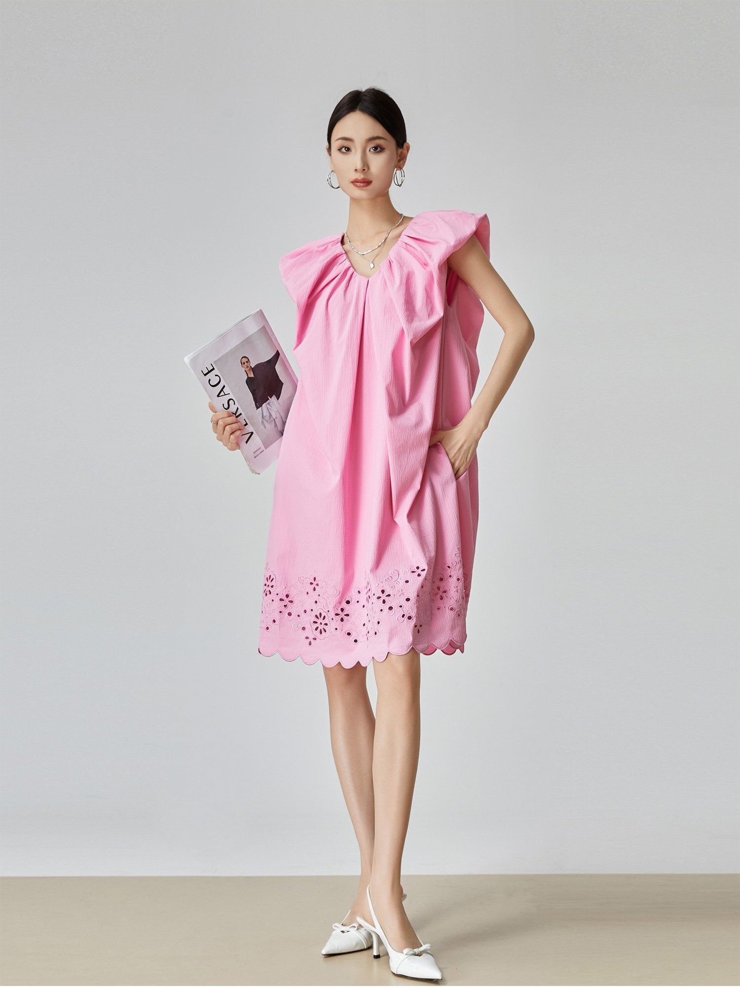 Woman wearing a pink dress holding a magazine on a plain background