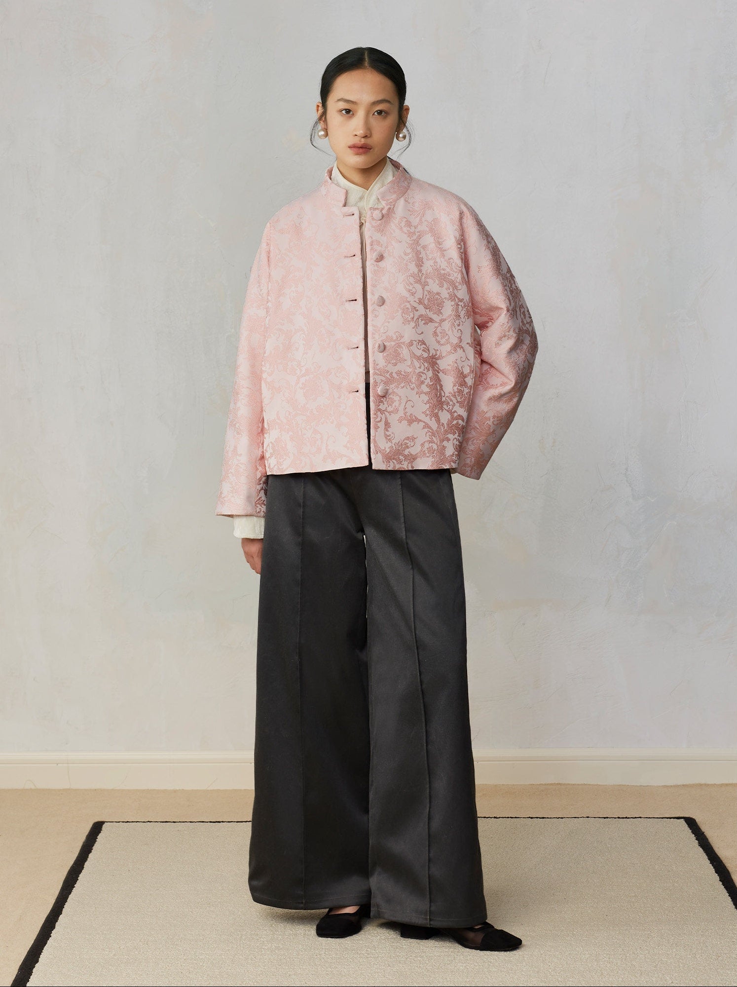 Person wearing a pink textured jacket and black pants against a plain background