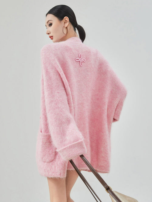 woman standing wearing a pink buckle cardigan against a plain background.  
