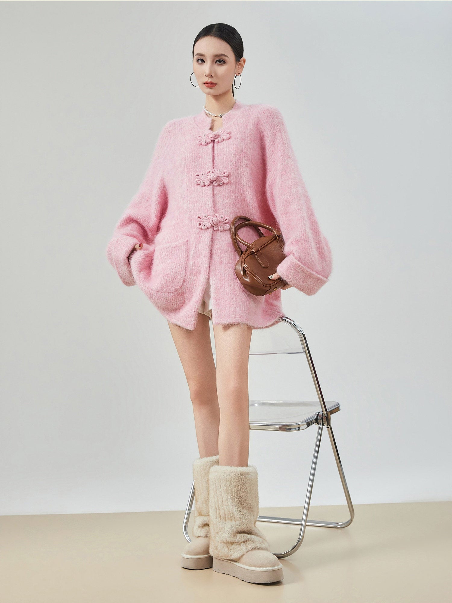 woman standing wearing a pink buckle cardigan against a plain background.  