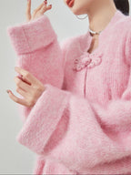 woman standing wearing a pink buckle cardigan against a plain background.  