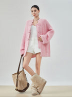 woman standing wearing a pink buckle cardigan against a plain background. 