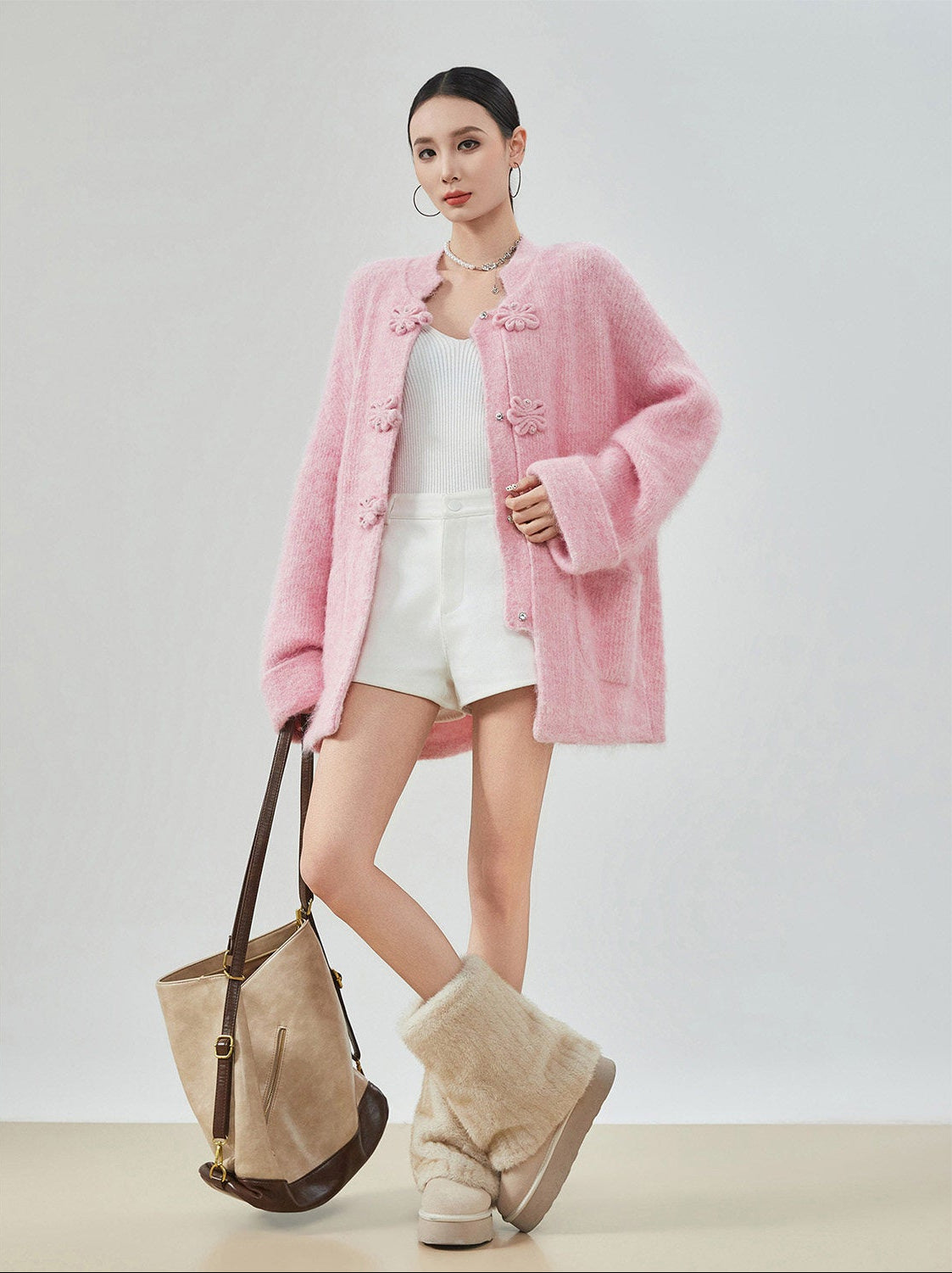 woman standing wearing a pink buckle cardigan against a plain background. 