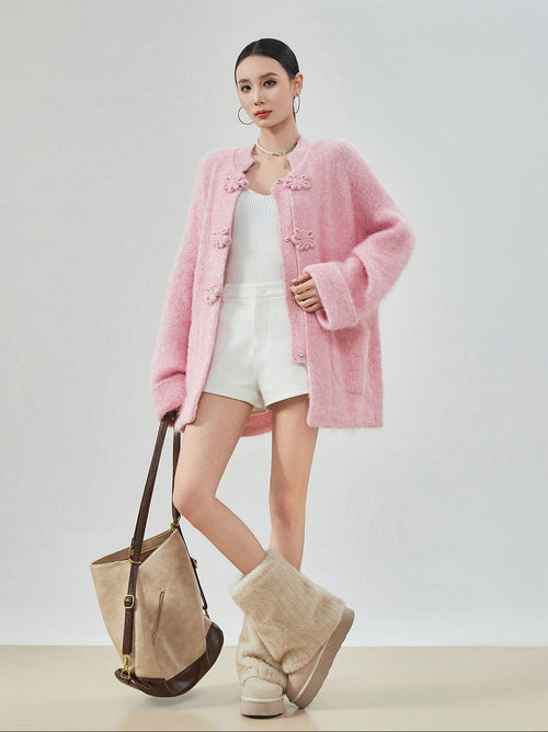 woman standing wearing a pink buckle cardigan against a plain background. 