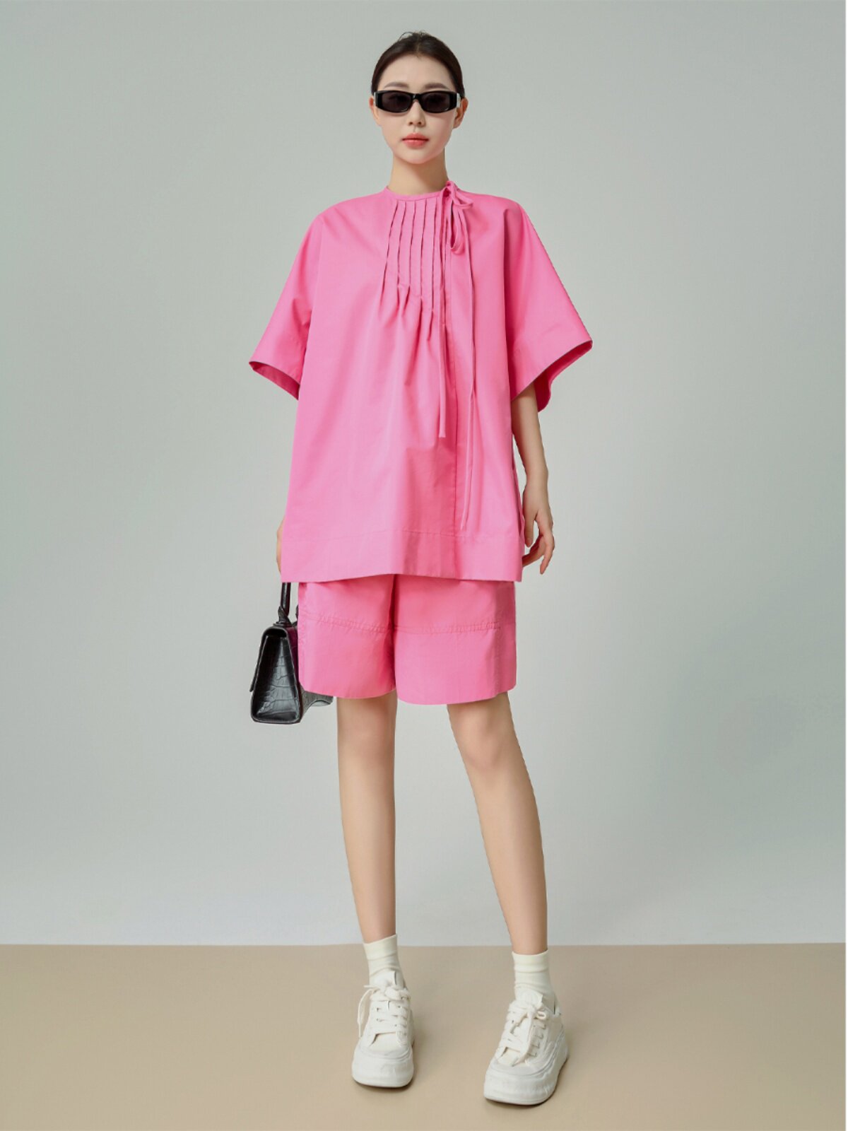 Person wearing a pink outfit with sunglasses against a plain background