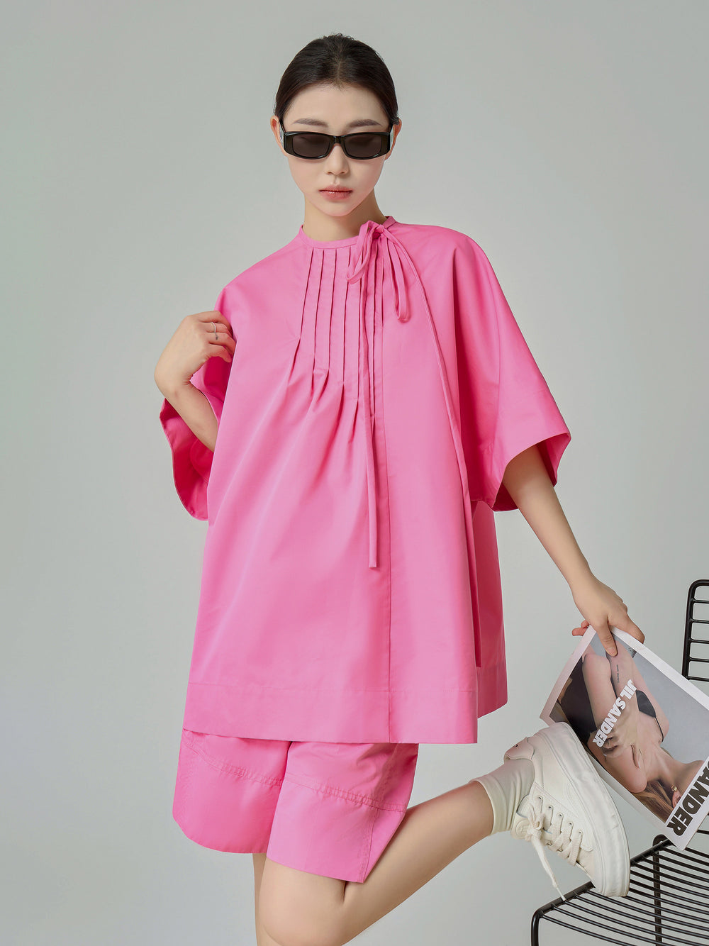 Person wearing a pink outfit with sunglasses on a plain background