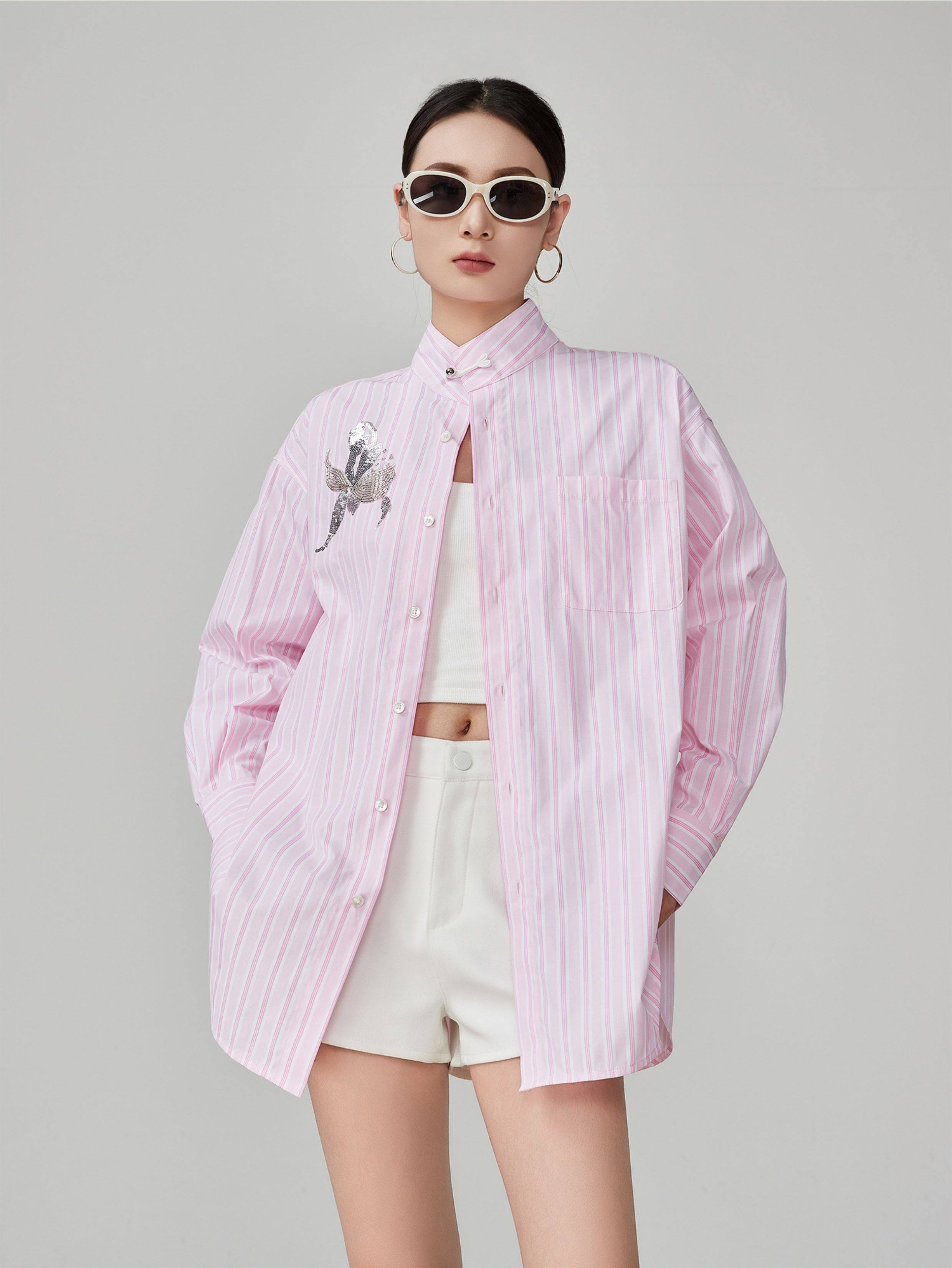 woman wearing a pink striped shirt with a white top and shorts on a gray background