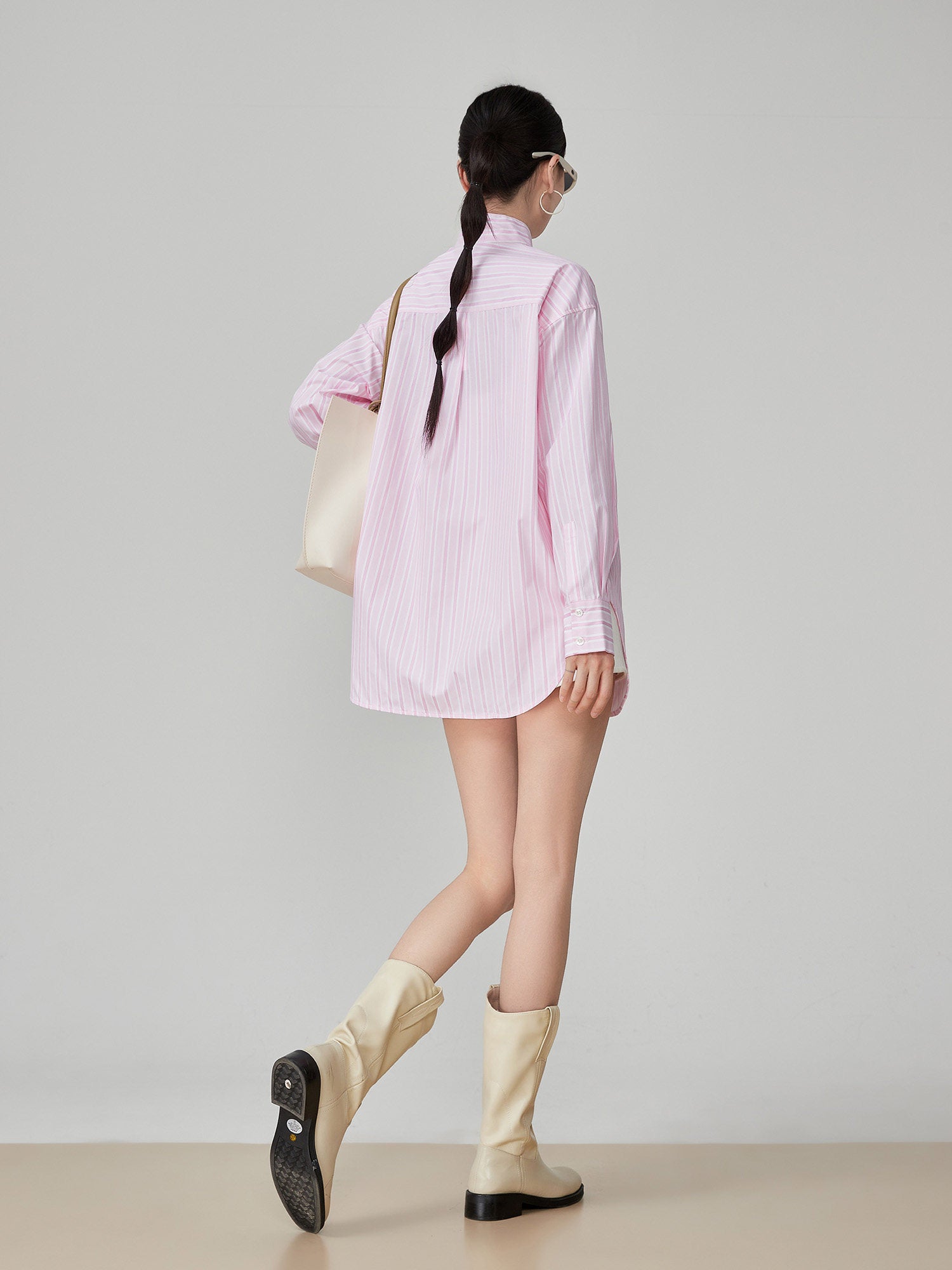 Woman wearing a pink striped shirt and beige knee-high boots on a plain background
